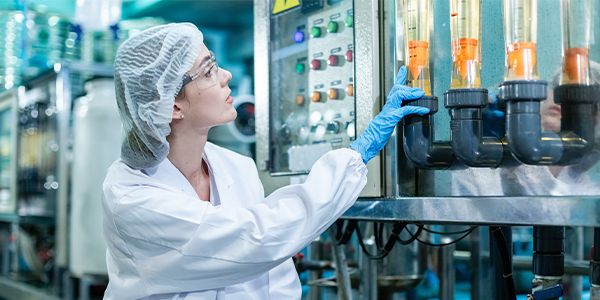 Technician in protective clothing operating a filtration control panel in a bottled water production facility.