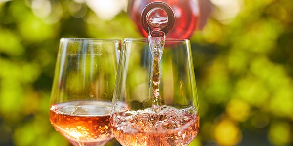 Wine being poured into two glasses outdoors.