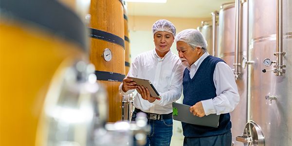 Winery workers inspecting a wine sample beside stainless steel filtration equipment.